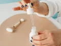 Dłoń z ciemnym lakierem do paznokci aplikuje serum z niacynamidem i kwasem salicylowym. Obok leży jadeitowy roller.