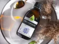 Olej z czarnuszki Olini, nierafinowany, tłoczony na zimno. Naturalny olejek na trądzik, zamknięty w szklanej butelce, otoczony suchymi trawami i złotą łyżeczką.