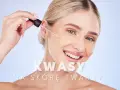 Kobieta z uśmiechem aplikuje kroplę serum z pipety. Kwasy na skórę twarzy to klucz do pięknej cery.