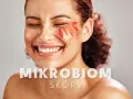 Uśmiechnięta kobieta z płatkami kwiatów na policzku. Tekst: "MIKROBIOM SKÓRY".