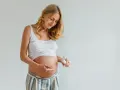 Ciężarna kobieta delikatnie wmasowuje krem z kwasem hialuronowym w brzuszek, dbając o skórę w tym wyjątkowym czasie.