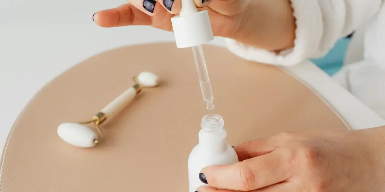 Dłoń z ciemnym lakierem do paznokci aplikuje serum z niacynamidem i kwasem salicylowym. Obok leży jadeitowy roller.