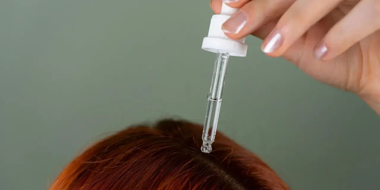 Dłoń z pipetką aplikuje serum na rudą skórę głowy. Idealne rozwiązanie, czym nawilżyć skórę głowy.