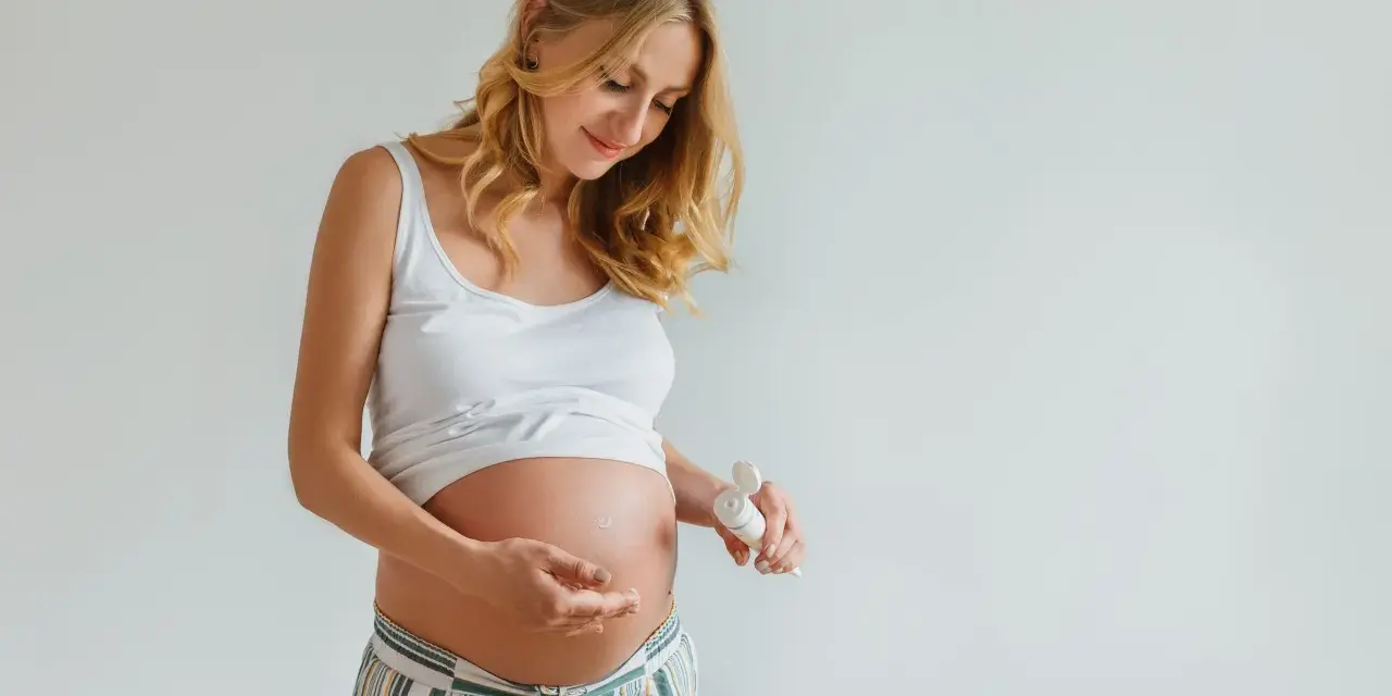 Ciężarna kobieta delikatnie wmasowuje krem z kwasem hialuronowym w brzuszek, dbając o skórę w tym wyjątkowym czasie.