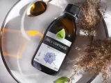 Olej z czarnuszki Olini, nierafinowany, tłoczony na zimno. Naturalny olejek na trądzik, zamknięty w szklanej butelce, otoczony suchymi trawami i złotą łyżeczką.