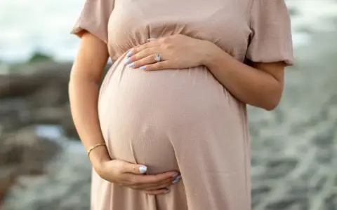 Kobieta w ciąży, która zastanawia się nad stosowaniem retinolu, delikatnie obejmuje swój brzuszek.