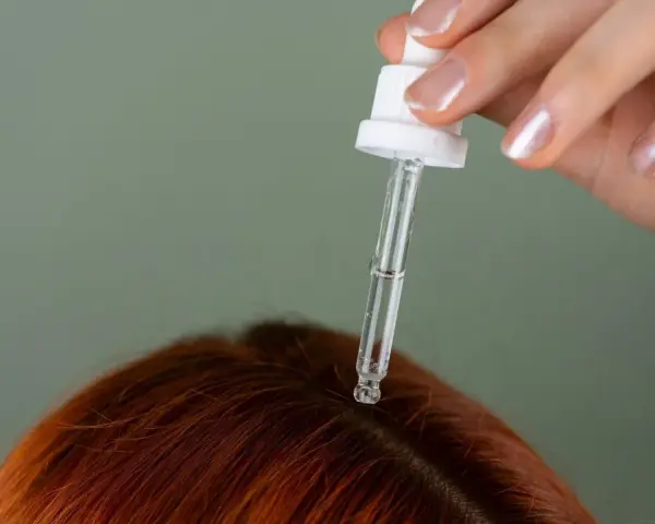 Dłoń z pipetką aplikuje serum na rudą skórę głowy. Idealne rozwiązanie, czym nawilżyć skórę głowy.
