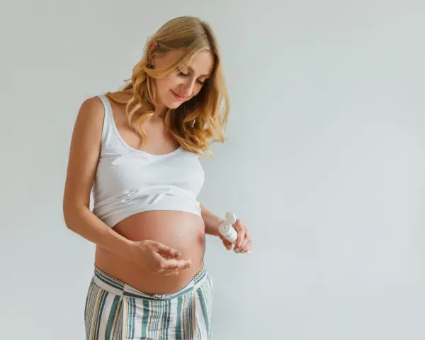 Ciężarna kobieta delikatnie wmasowuje krem z kwasem hialuronowym w brzuszek, dbając o skórę w tym wyjątkowym czasie.