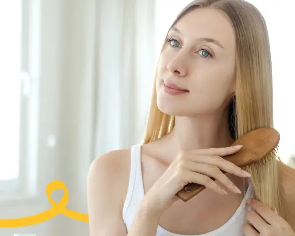 Kobieta szczotkuje długie blond włosy, przygotowując się do domowego peelingu skóry głowy.