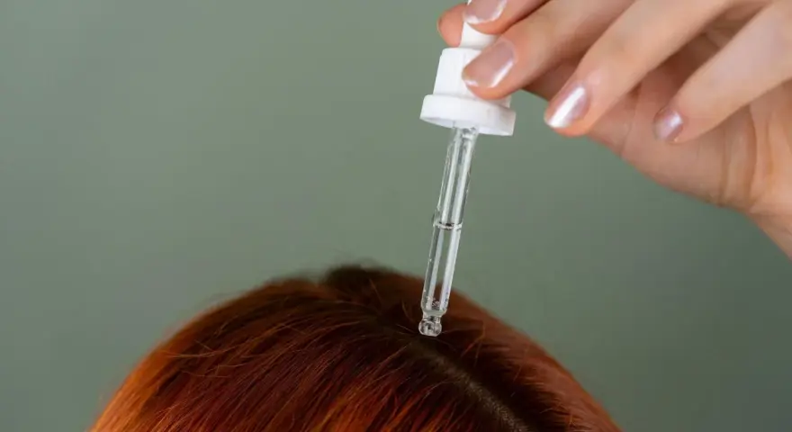 Dłoń z pipetką aplikuje serum na rudą skórę głowy. Idealne rozwiązanie, czym nawilżyć skórę głowy.