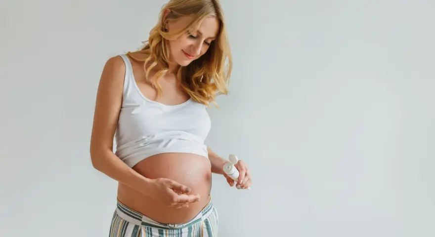 Ciężarna kobieta delikatnie wmasowuje krem z kwasem hialuronowym w brzuszek, dbając o skórę w tym wyjątkowym czasie.