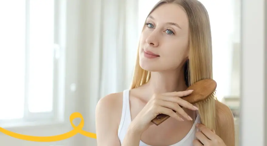 Kobieta szczotkuje długie blond włosy, przygotowując się do domowego peelingu skóry głowy.
