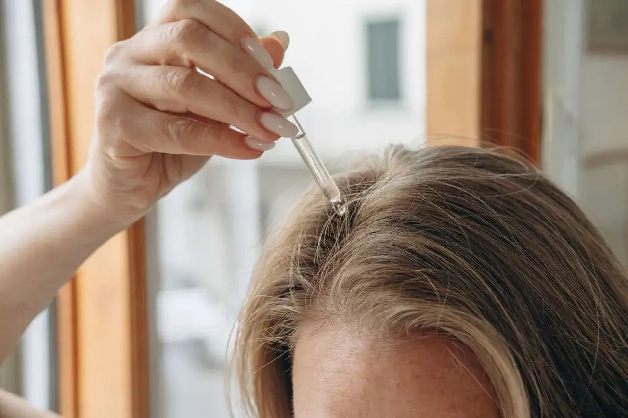 Dłoń z pipetką aplikuje serum na skórę głowy. To sposób, czym nawilżyć skórę głowy, by włosy były zdrowsze.