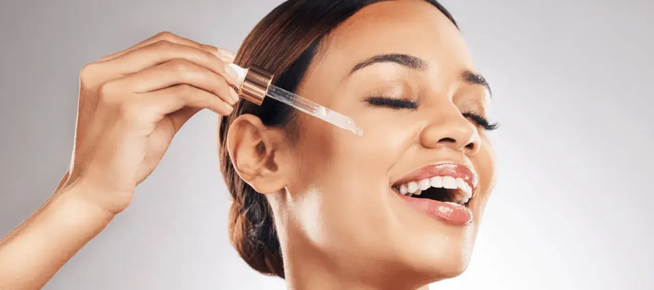 Kobieta aplikuje serum z pipetki na twarz. Skóra promienieje, a uśmiech sugeruje, że to skuteczny retinol na zmarszczki.